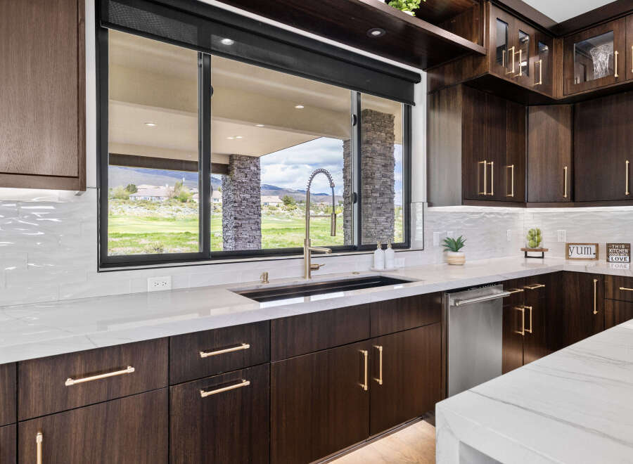 This stunning kitchen boasts modern dark wood cabinetry with sleek gold hardware, complemented by a large window offering picturesque views.