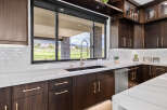 This stunning kitchen boasts modern dark wood cabinetry with sleek gold hardware, complemented by a large window offering picturesque views.