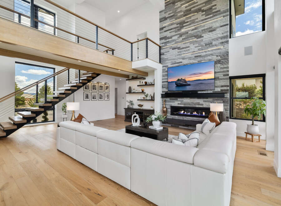 Stunning modern living room with a floor-to-ceiling stone fireplace, large windows offering scenic views, and a spacious open floor plan.