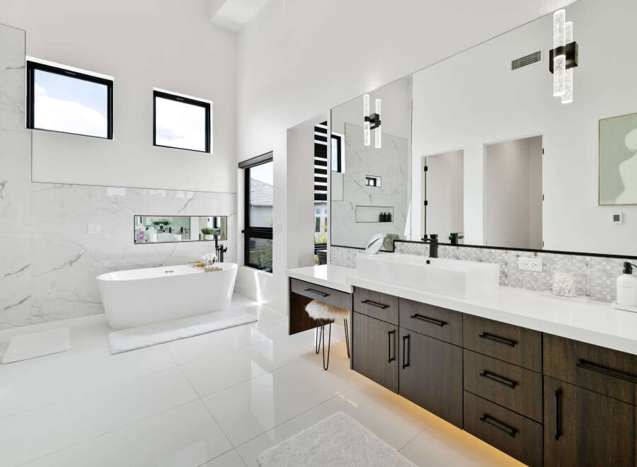 Luxurious master bathroom boasts a freestanding soaking tub, double vanity with dark wood cabinets, and marble tile.