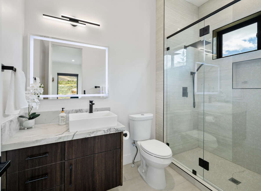 This stunning bathroom boasts modern design elements, including a sleek, frameless glass shower enclosure and a marble-topped vanity with dark wood cabinetry.