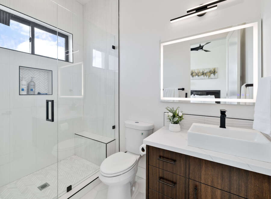 This stunning bathroom boasts a spacious shower with a built-in bench and herringbone tile floor, complemented by a sleek, modern vanity with dark wood cabinetry and a quartz countertop.