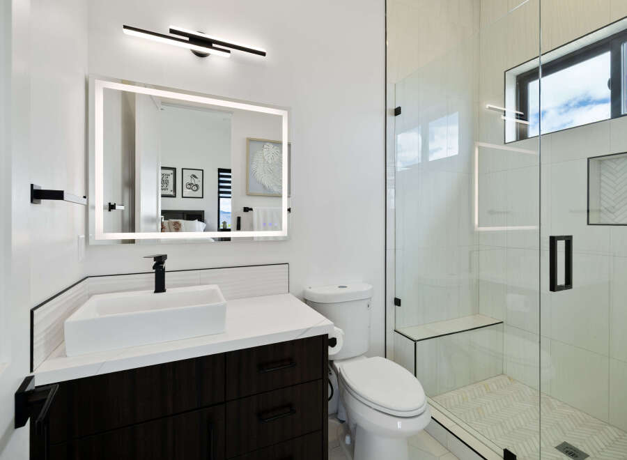 This stunning bathroom boasts a modern design with sleek dark cabinetry, a frameless glass shower, and a white quartz countertop.