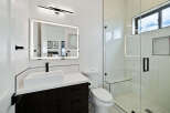 This stunning bathroom boasts a modern design with sleek dark cabinetry, a frameless glass shower, and a white quartz countertop.