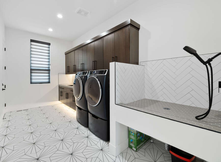 This stunning laundry room boasts modern dark wood cabinets, geometric patterned flooring, and a built-in pet washing station.