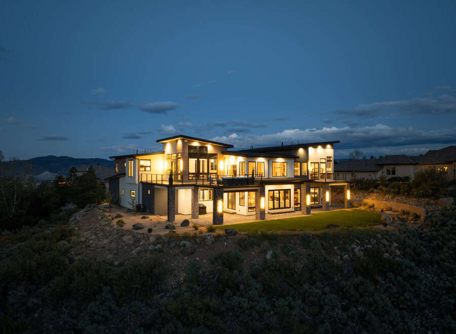 Stunning modern home nestled on a hillside, boasting expansive windows and a spacious backyard.