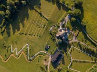 This stunning property boasts a unique design, featuring a winding pathway, expansive green lawns, and a charming main house.