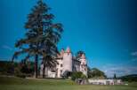 This stunning property boasts a majestic castle with three imposing towers, surrounded by lush greenery and a clear blue sky.