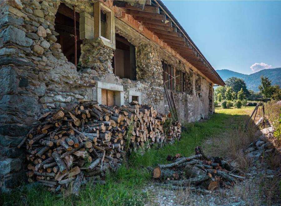 Rustic stone house with woodpile, undergoing renovation.
