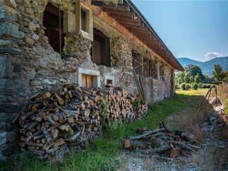 Rustic stone house with woodpile, undergoing renovation.
