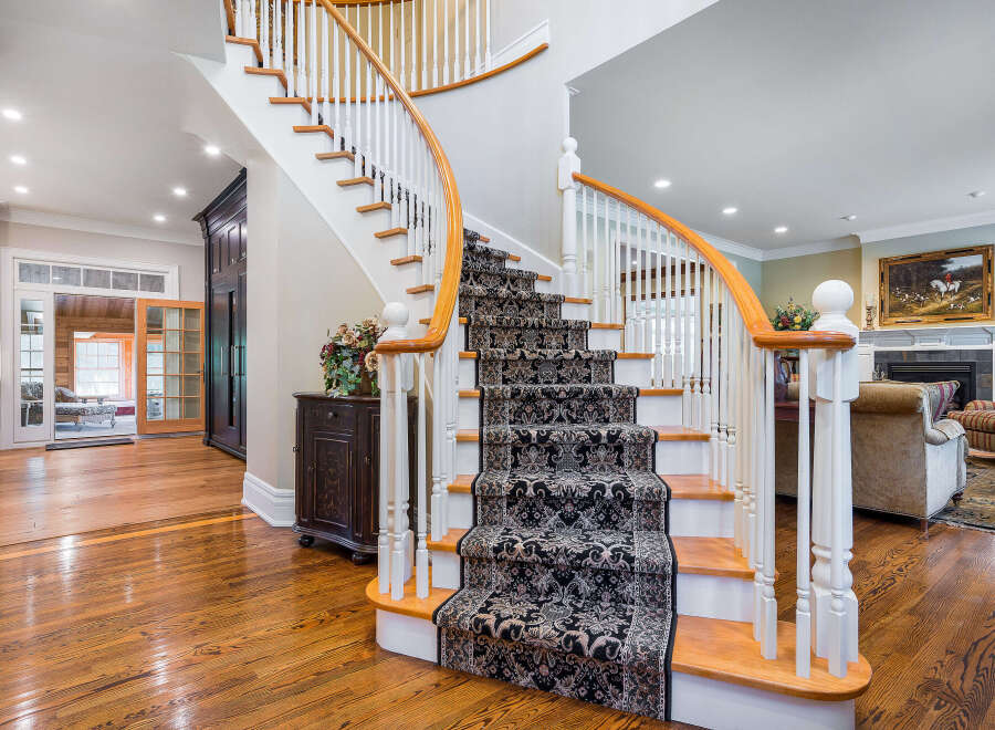 Elegant curved staircase with ornate runner, hardwood floors throughout, and a view into a sunlit sunroom.
