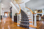 Elegant curved staircase with ornate runner, hardwood floors throughout, and a view into a sunlit sunroom.