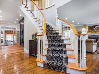 Elegant curved staircase with ornate runner, hardwood floors throughout, and a view into a sunlit sunroom.