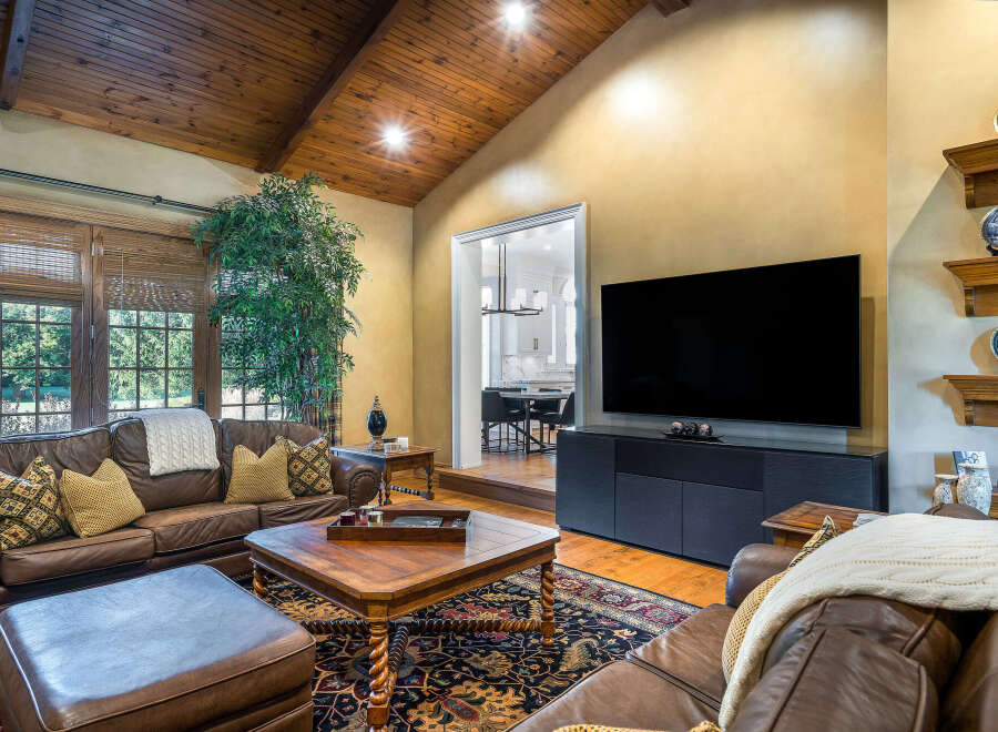 This stunning living room boasts a gorgeous wood-beamed ceiling, large windows offering ample natural light, and a cozy leather seating area perfect for relaxation.