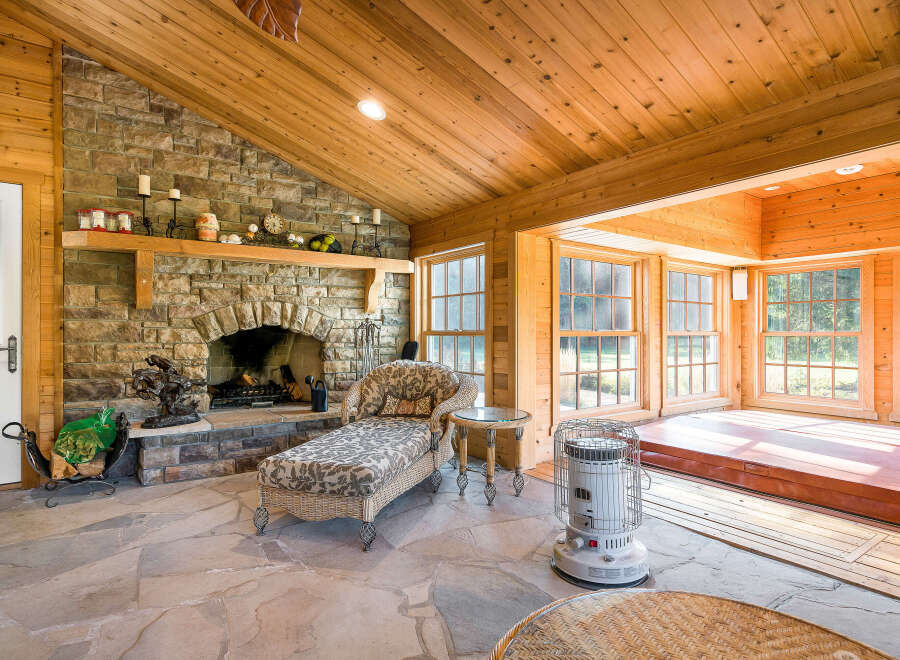 This sunroom boasts a stunning stone fireplace, vaulted wood ceilings, and expansive windows offering abundant natural light.