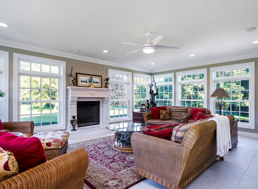 Sun-drenched sunroom boasts a cozy wicker furniture arrangement, complemented by a fireplace and large windows offering scenic views.