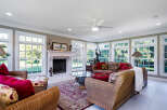 Sun-drenched sunroom boasts a cozy wicker furniture arrangement, complemented by a fireplace and large windows offering scenic views.