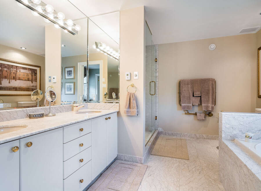 This luxurious bathroom boasts a double vanity with marble countertops and gold accents, complemented by large mirrors and ample storage.