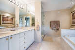 This luxurious bathroom boasts a double vanity with marble countertops and gold accents, complemented by large mirrors and ample storage.