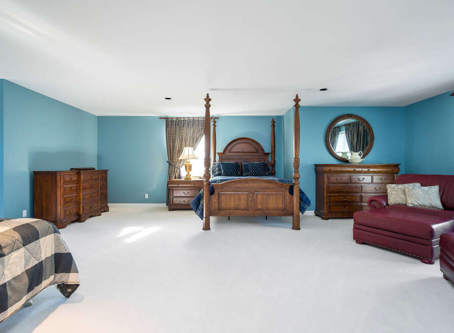 Spacious master bedroom with plush carpeting, featuring a four-poster bed and ample built-in storage.