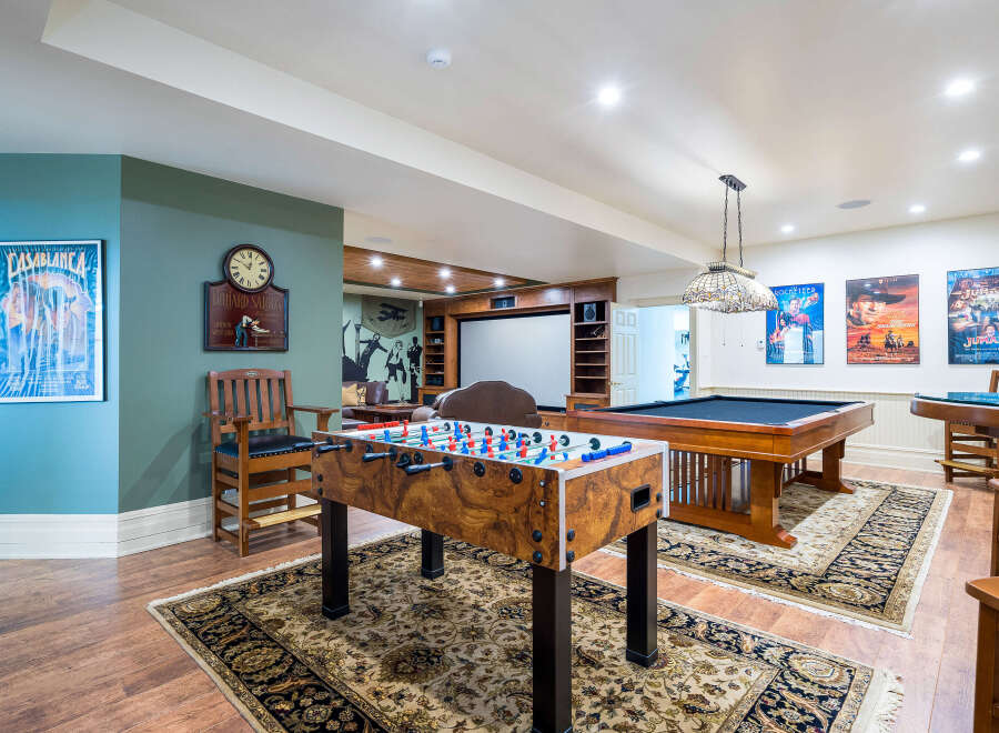 This stunning game room boasts a classic billiards table, foosball table, and a home theater, perfect for entertaining guests.