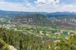 Panoramic view of a lush green valley with a meandering river, surrounded by majestic mountains under a vibrant blue sky.