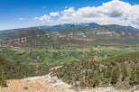 Panoramic view of a picturesque valley with a meandering river, lush green fields, and a backdrop of majestic mountains.