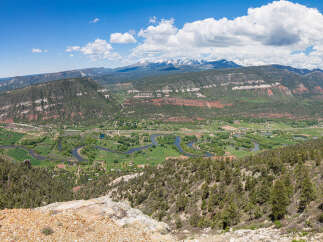 Panoramic view of a picturesque valley with a meandering river, lush green fields, and a backdrop of majestic mountains.