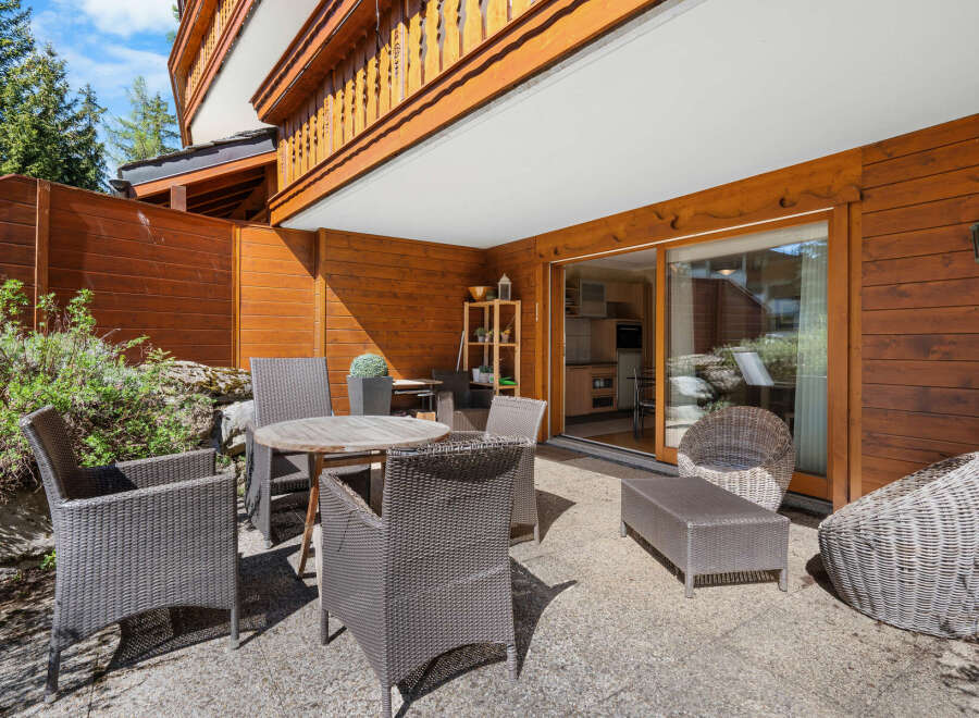This stunning property boasts a spacious patio perfect for outdoor dining and relaxation, complete with comfortable wicker furniture and a wooden table.