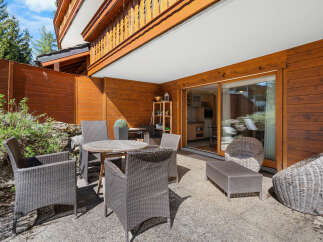 This stunning property boasts a spacious patio perfect for outdoor dining and relaxation, complete with comfortable wicker furniture and a wooden table.