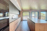 Modern kitchen with sleek dark cabinets and light wood countertops, offering stunning views through large windows.