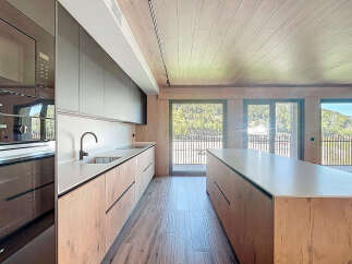Modern kitchen with sleek dark cabinets and light wood countertops, offering stunning views through large windows.