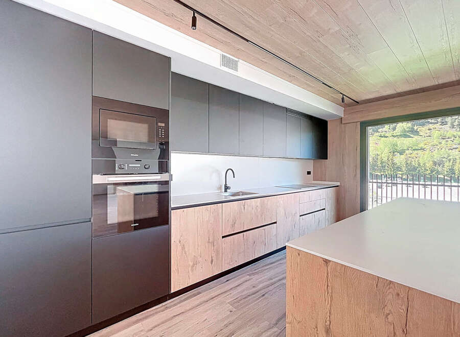 Modern kitchen with sleek dark gray cabinets and wood countertops, offering a stunning view of a mountain landscape through large windows.