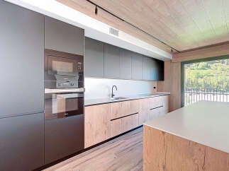 Modern kitchen with sleek dark gray cabinets and wood countertops, offering a stunning view of a mountain landscape through large windows.