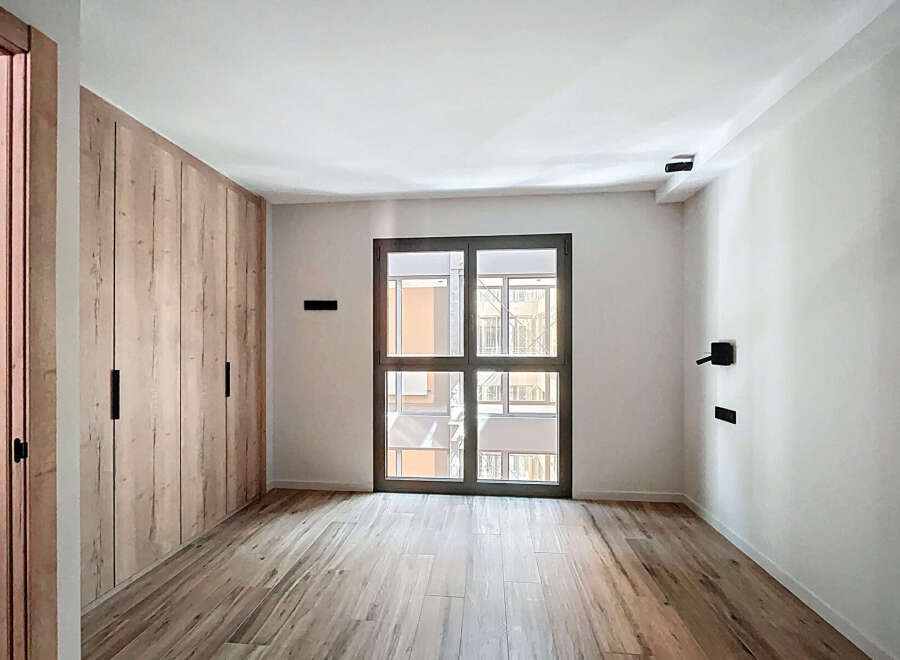 Bright and airy bedroom with built-in wooden wardrobe and large window offering ample natural light.
