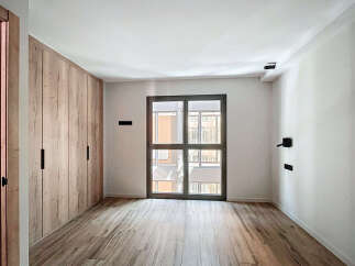 Bright and airy bedroom with built-in wooden wardrobe and large window offering ample natural light.