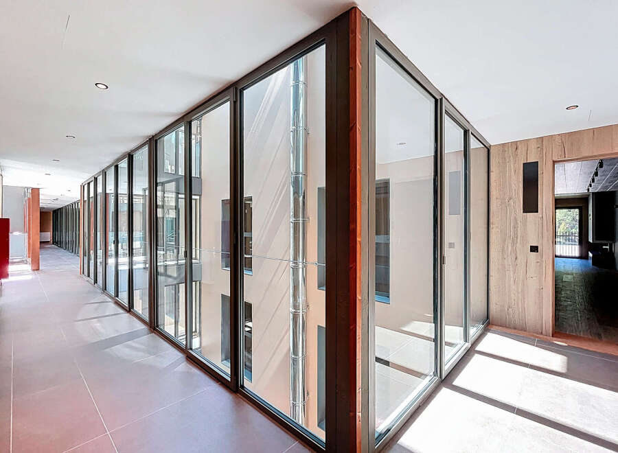 Modern hallway with floor-to-ceiling glass walls offering abundant natural light and views of an inner courtyard.