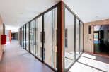 Modern hallway with floor-to-ceiling glass walls offering abundant natural light and views of an inner courtyard.