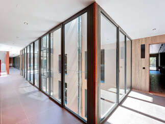 Modern hallway with floor-to-ceiling glass walls offering abundant natural light and views of an inner courtyard.