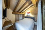 Cozy chalet bedroom with wooden beams, a comfortable bed, and a wall-mounted TV.