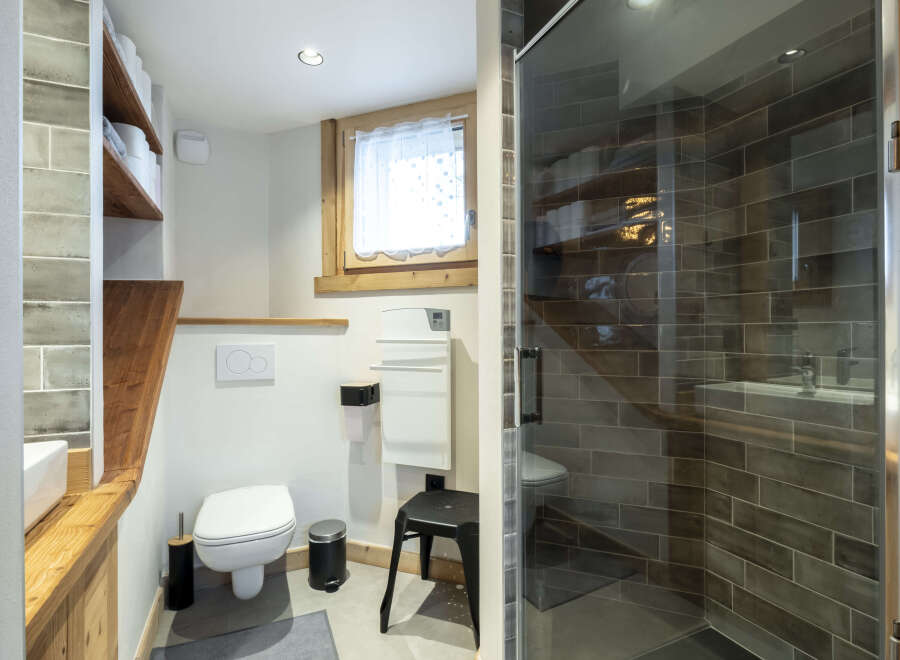 Modern bathroom with a walk-in shower, wooden shelving, and stylish gray tile flooring.