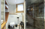 Modern bathroom with a walk-in shower, wooden shelving, and stylish gray tile flooring.