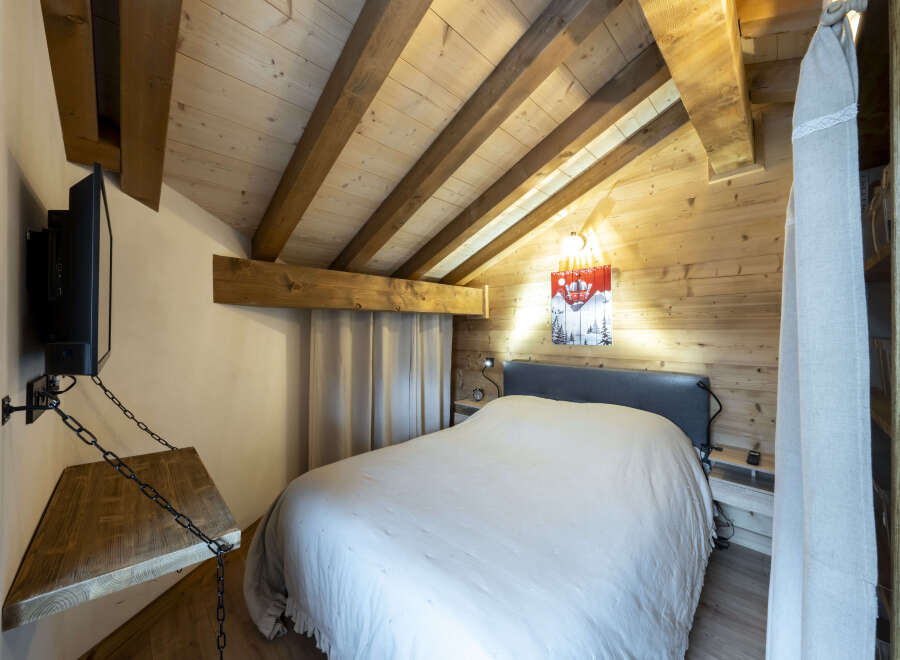 Cozy chalet bedroom with wooden beams, a comfortable bed, and a wall-mounted TV.
