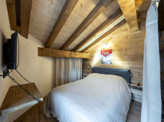 Cozy chalet bedroom with wooden beams, a comfortable bed, and a wall-mounted TV.