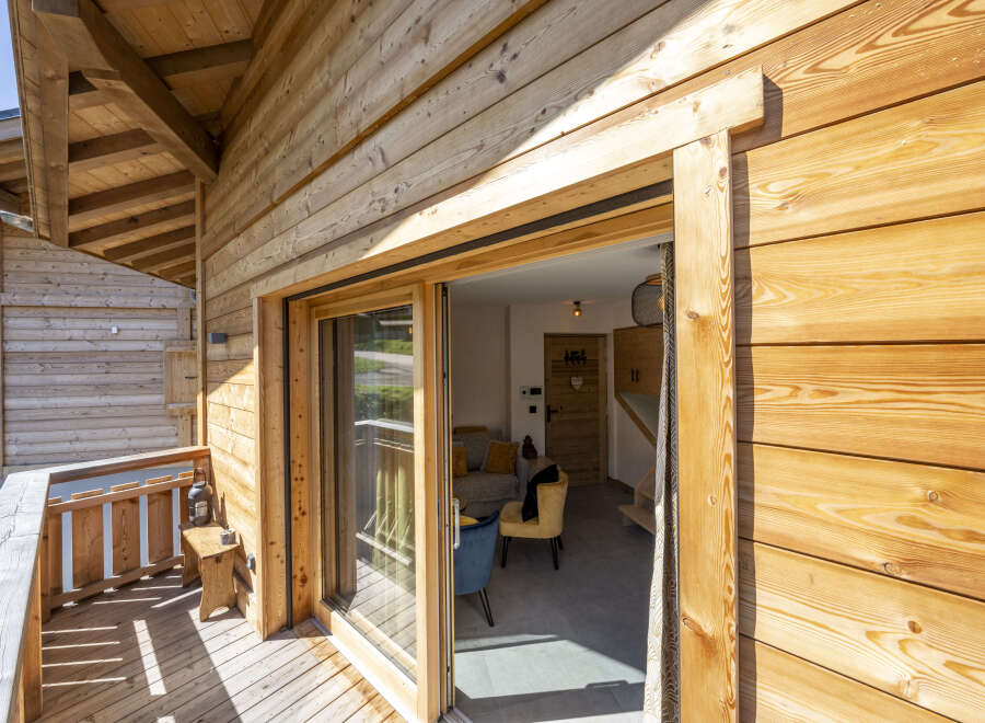 This stunning chalet boasts a spacious balcony with wooden decking, perfect for enjoying the mountain views.