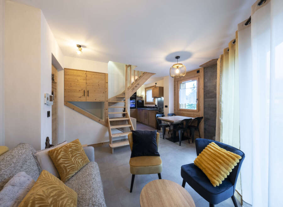 Cozy living room with a modern and rustic design, featuring a comfortable sofa, armchairs, and a wooden staircase.