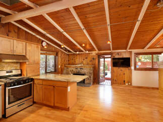 This charming cabin boasts a spacious kitchen with granite countertops and wooden cabinetry, complemented by a cozy stone fireplace.