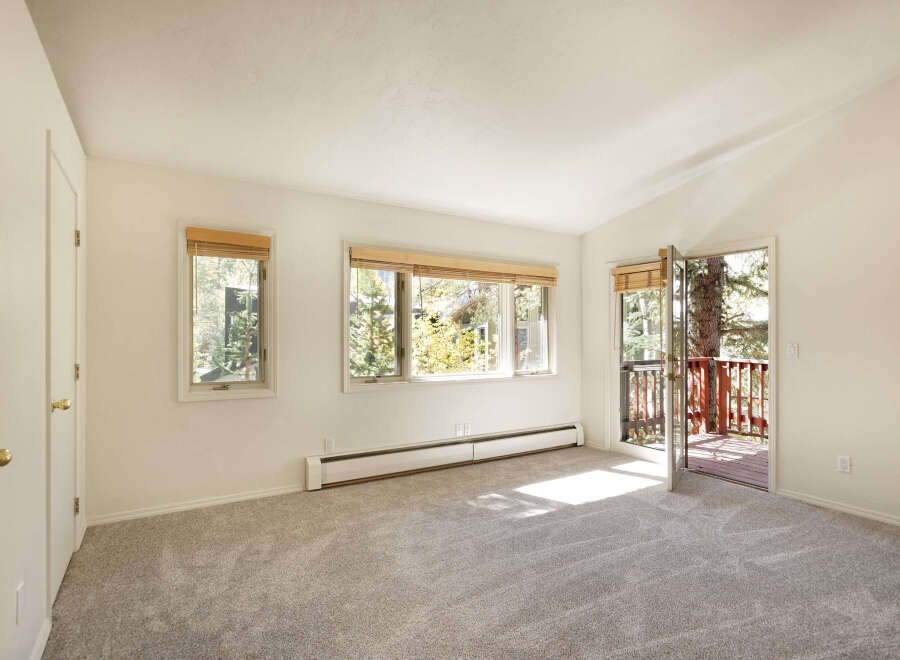 Bright and spacious bedroom with plush carpeting, large windows offering abundant natural light, and a private balcony access.