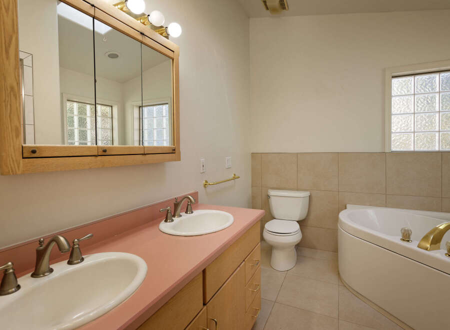 This charming bathroom boasts a double vanity with pink countertop and updated sink and faucet fixtures.