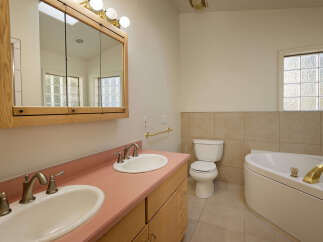 This charming bathroom boasts a double vanity with pink countertop and updated sink and faucet fixtures.